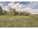 Spacious property with ample grass and a home surrounded by mature trees beneath a blue sky with fluffy white clouds at 4346 S Quail St, Littleton, CO 80127