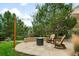 Backyard stone patio with cozy fire pit surrounded by mature trees and lush landscaping at 15348 W 75Th Pl, Arvada, CO 80007