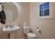 Charming half bathroom features a pedestal sink, toilet, round mirror, and window with shutter at 6358 S Miller Way, Littleton, CO 80127