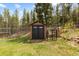 A backyard storage shed is constructed with wooden siding, set on a small concrete foundation near a greenhouse at 8600 S Warhawk Rd, Conifer, CO 80433