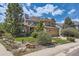 Tan and stone two-story home showcasing a lush lawn and mature trees at 7083 Turweston Ln, Castle Pines, CO 80108
