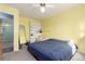 Bedroom with yellow walls, light carpet, blue bedspread, shelving unit, and a view to bathroom at 15492 E Floyd Ave, Aurora, CO 80013