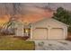 Tan home featuring an attached two-car garage, front lawn, and mature trees under a colorful dusk sky at 11623 W Hornsilver Mtn, Littleton, CO 80127
