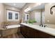Bathroom featuring a double sink vanity, soaking tub, and travertine tile surround at 10660 Winding Pine Pt, Highlands Ranch, CO 80126