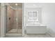 Modern bathroom with a glass-enclosed shower, freestanding soaking tub, bright window, and neutral tile flooring at 7291 Prairie Sage Pl, Littleton, CO 80125
