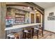 Cozy wet bar area with a stone wall, wooden beams, stocked shelves, and three stools at 242 Point View Pl, Breckenridge, CO 80424