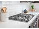 A close up on the modern stovetop, surrounded by quartz counters and white subway tile at 9700 E 63Rd Pl, Denver, CO 80238