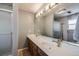 Well-lit bathroom featuring double sinks, wood cabinets, and a glass-enclosed shower at 6323 W Rowland Cir, Littleton, CO 80128