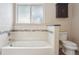 Bright bathroom featuring a white tub with tile accents, a toilet, and an overhead cabinet at 7650 W 24Th Ave, Lakewood, CO 80214
