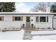 Charming single-story home featuring white brick, a gray door and shutters and a snow-covered front yard at 13438 W 23Rd Pl, Golden, CO 80401