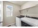 Bright laundry room featuring modern washer and dryer units, window, and storage shelf at 19131 E 65Th Ave, Denver, CO 80249