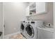 Well-lit laundry room with modern washer and dryer, white cabinets, and tile flooring at 6893 Decatur St, Denver, CO 80221