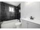 Modern bathroom featuring sleek, black tile, white fixtures, and a shower-tub combination at 7977 Durango St, Denver, CO 80221
