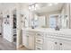 Neutral-toned bathroom featuring dual sinks, white cabinetry, and a glimpse into the walk-in closet at 11938 S Meander Way, Parker, CO 80138