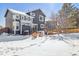 View of the gray two-story home from the snow-covered backyard with a wood deck and outdoor seating area at 4241 Brookwood Pl, Highlands Ranch, CO 80130