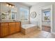 Bright bathroom featuring a soaking tub, wood cabinets, and a large window at 6273 Torrey Ln, Arvada, CO 80403