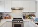 Bright kitchen featuring stainless steel range and hood, white cabinetry, subway tile backsplash, and ample counter space at 9400 E Iliff Ave # 145, Denver, CO 80231