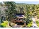 An elevated view of a brick two-story home with deck, surrounded by mature trees, blending into the natural landscape at 25357 Snyder Ave, Conifer, CO 80433