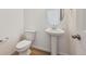 Cozy half-bath features a pedestal sink, round mirror, toilet, wood floors, and crisp white paint at 190 Lark Sparrow Way, Bennett, CO 80102