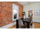 Dining room with exposed brick wall, a large window, and a dark wood table with seating for four at 2527 W Dunkeld Pl, Denver, CO 80211
