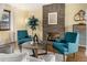 This living room is staged with two blue armchairs, a brick fireplace, a marble coffee table and hardwood floors at 7238 W Cedar Cir, Lakewood, CO 80226