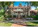 Elegant brick home featuring a rounded balcony, red tile roof, mature trees, and landscaped front yard at 3309 E 7Th Ave Pkwy, Denver, CO 80206