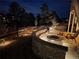 Cozy backyard patio featuring a stone fire pit, seating, and retaining wall with landscape lighting at night at 3131 Keepsake Way, Castle Rock, CO 80109