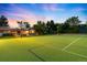 Lit tennis court at dusk, surrounded by mature trees and a glimpse of the pool area, perfect for evening play at 6211 E Orchard Dr, Greenwood Village, CO 80111