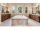 Bright bathroom featuring a large soaking tub with tile surround and dual vanities, illuminated by natural light from three windows at 6303 Ellingwood Point Pl, Castle Rock, CO 80108