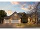 Beautiful stone home featuring a three-car garage and meticulously maintained landscaping under a dynamic, colorful sky at 21231 E Saddle Rock Ln, Aurora, CO 80016