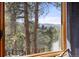 Stunning view of the mountains and forest through a window overlooking a deck with wooden railing at 7395 Heiter Hill Dr, Evergreen, CO 80439