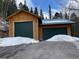A detached garage with two bays and green doors sits at the end of a snow-lined driveway at 32094 Christopher Ln, Conifer, CO 80433