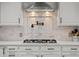 Close-up of a gas range with a stylish backsplash and modern vent hood at 7862 Stonedale Dr, Castle Pines, CO 80108