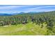Stunning aerial view of a home nestled in a verdant meadow surrounded by trees and rolling hills at 26085 Amy Cir, Conifer, CO 80433