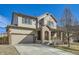 Two story home with tan siding, brick porch detail, large garage and manicured lawn at 5177 Delphinium Cir, Brighton, CO 80601