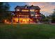 A home at dusk featuring multiple decks with red pergolas, manicured lawns, landscape lighting, and exterior stone accents at 1300 W Caley Ave, Littleton, CO 80120