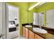 Well-lit bathroom with a double sink vanity, large mirror, and bright green accent wall at 13325 W 86Th Dr, Arvada, CO 80005