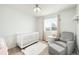Cozy Bedroom showcasing a white crib, gray armchair, and soft natural light from the window at 10906 Pastel Pt, Parker, CO 80134