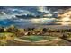 A high-angle view features a well-maintained green tennis court under a dramatic sky and mountain backdrop at 19770 E Geddes Pl, Centennial, CO 80016