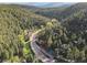 Majestic aerial view featuring the property and its tranquil wooded surroundings with a road and mountains in the distance at 27383 Highway 74, Evergreen, CO 80439