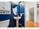 Powder room featuring blue textured walls, pedestal sink, oval mirror, and hardwood floors at 1063 Roslyn Ct, Denver, CO 80230