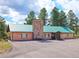 Single-story brick building with a green metal roof and stone chimney, set against a blue sky at 439 Ronnie Rd, Golden, CO 80403