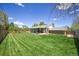 Expansive backyard view of a brick house with a covered patio, overlooking a lush, green lawn and wooded fence at 1733 S Urban Way, Lakewood, CO 80228