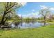 Scenic view of a tranquil pond with lush green grass, mature trees, and reflections on the water at 10868 W 70Th Ave, Arvada, CO 80004