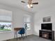 Bedroom featuring gray carpet, ceiling fan, two windows with blinds and a TV sitting on an electric fireplace at 5045 Preserve Pl, Firestone, CO 80504