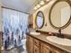 Functional bathroom featuring double sinks, oval mirrors and a shower with blue-toned curtain at 11002 E Ohio Pl, Aurora, CO 80012