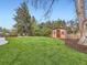 Backyard featuring a vibrant lawn, mature trees, landscaping, and storage shed at 6768 Vivian St, Arvada, CO 80004