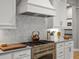 Close-up of a kitchen with white cabinets and a stainless steel gas range and custom vent hood at 9035 S Shawnee Ct, Aurora, CO 80016