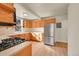 Well-lit kitchen features stainless steel refrigerator, gas range, wood cabinets, light countertops and tile backsplash at 2015 Elmira St, Aurora, CO 80010