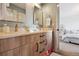 Bright bathroom featuring double sinks, wooden cabinetry, and a doorway leading to a bedroom at 17490 W 67Th Ave, Arvada, CO 80007